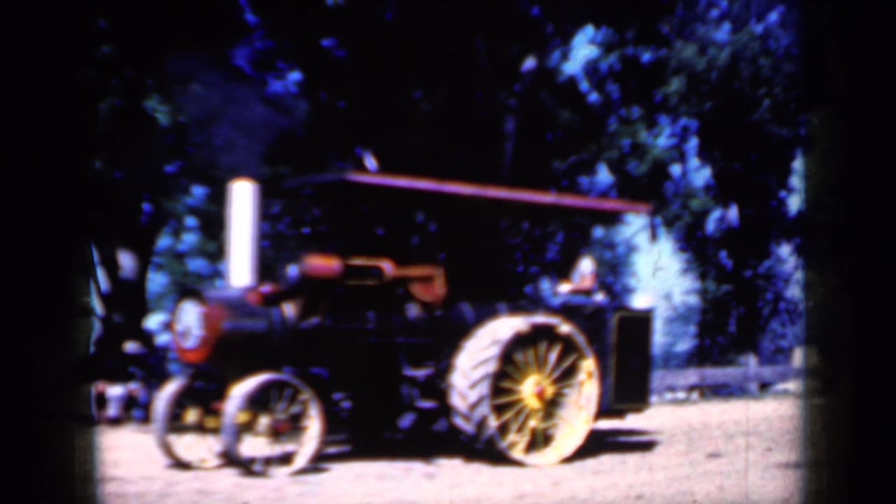 Side view of the Iowa steam traction engine in 1959, with a bright smokestack and large spoked rear wheel visible under trees.