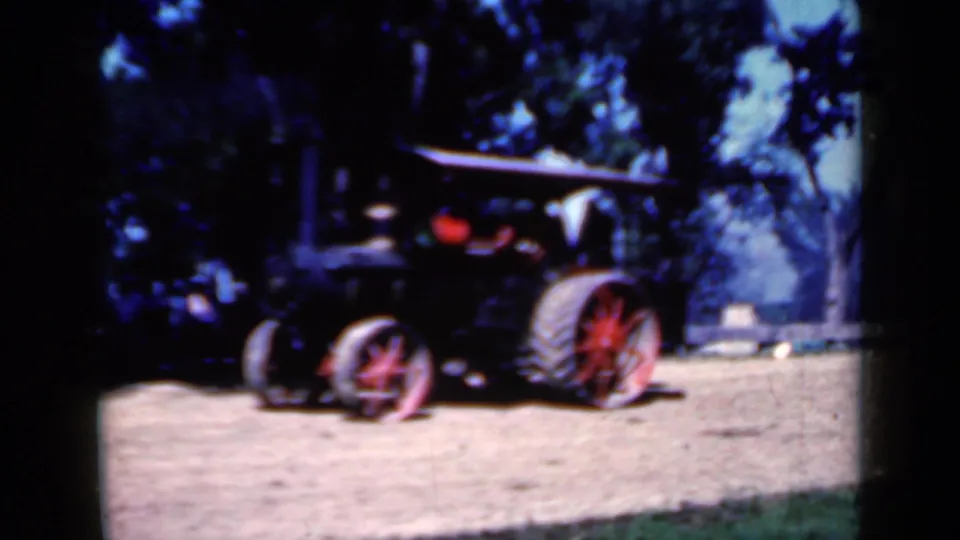 Final 1959 Iowa frame of the steam traction engine partly in shade, showing its red wheel, large rear wheel, and leafy fairground setting.