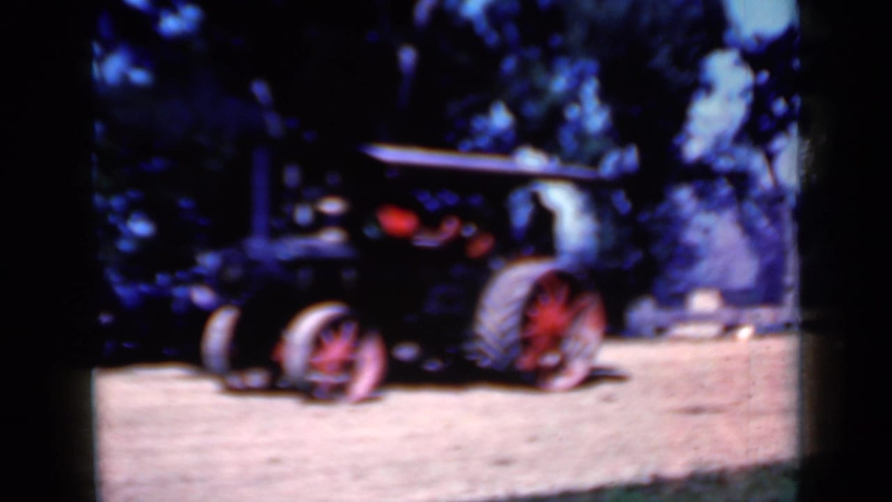 Steam tractor with red wheels moving across a dirt field beside trees.