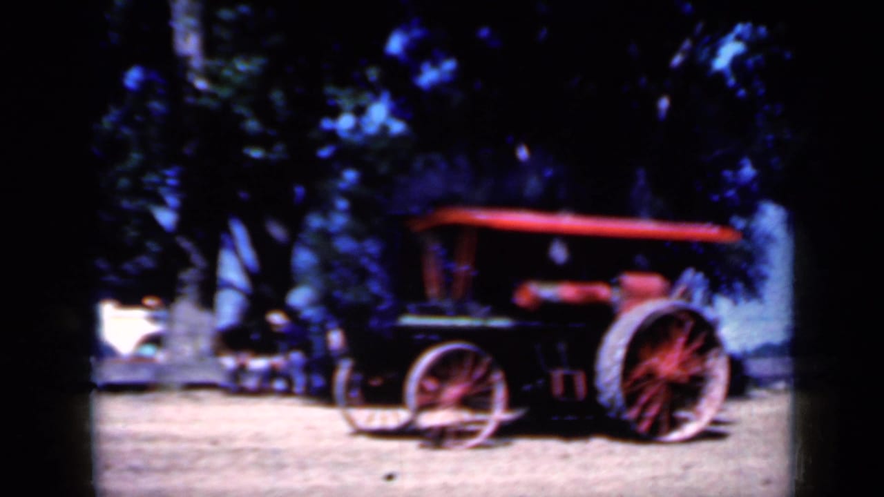 1959 Iowa 8mm frame with the steam tractor in side view, red canopy and wheels visible, and smoke rising near a tree-lined background.