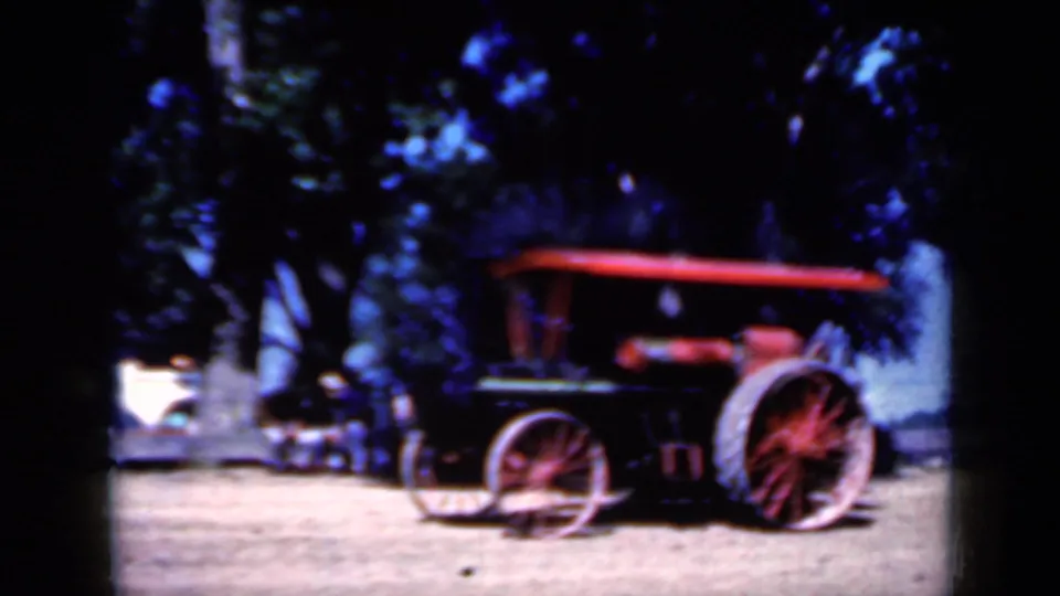1959 Iowa 8mm frame with the steam tractor in side view, red canopy and wheels visible, and smoke rising near a tree-lined background.