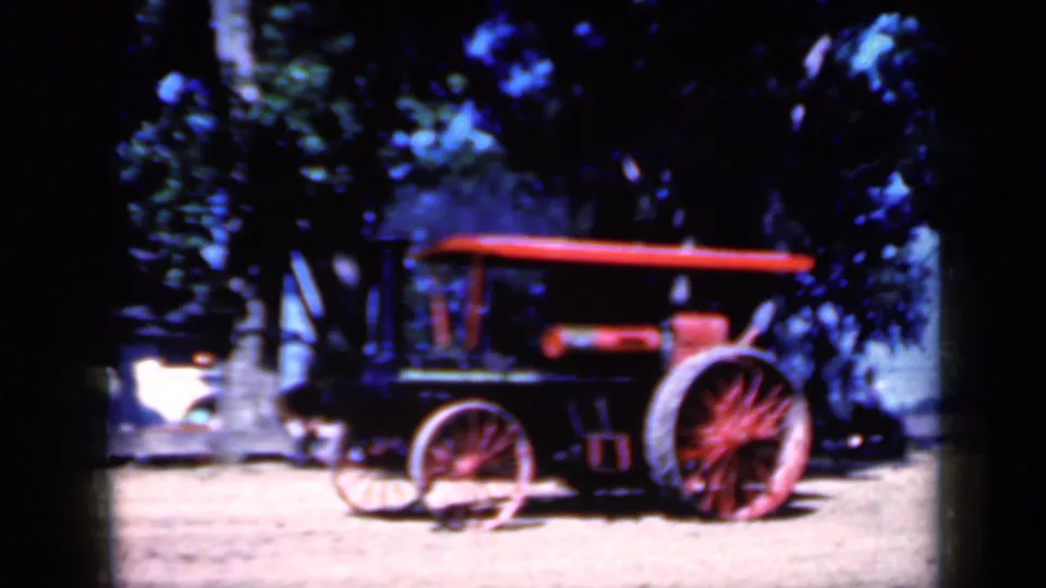 1959 Iowa 8mm frame showing the steam tractor centered, its red wheels and canopy standing out against trees and bright ground.