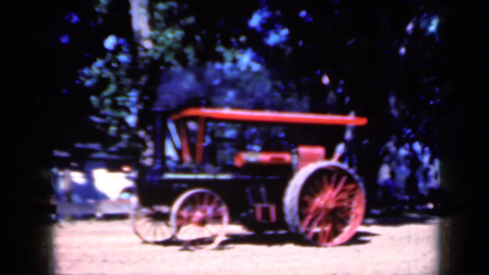1959 Iowa 8mm frame showing the steam tractor farther right, with a dark smoke plume above the canopy and trees behind it.