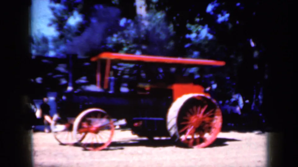 Closer 1959 Iowa home-movie view of a steam-powered tractor on a dirt road with bystanders partly visible at left.