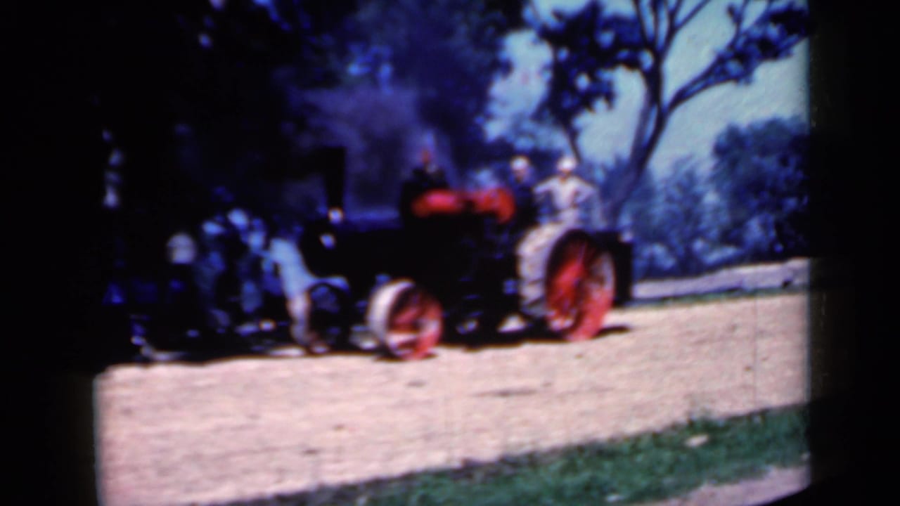 Black tractor with red wheels approaches on a dirt path with smoke rising behind it.