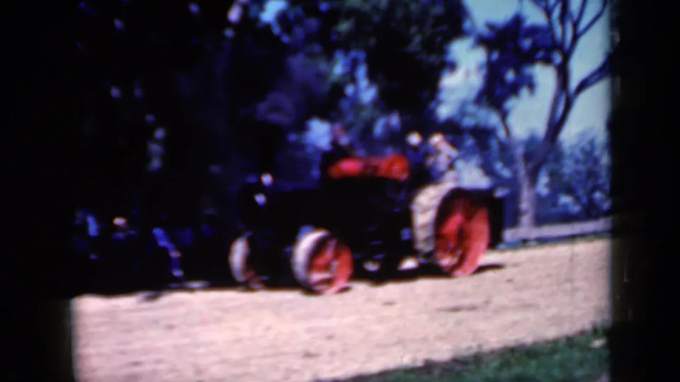 The tractor appears closer in the frame, its red wheels prominent while smoke and trees remain visible in the 1959 Iowa rural scene.