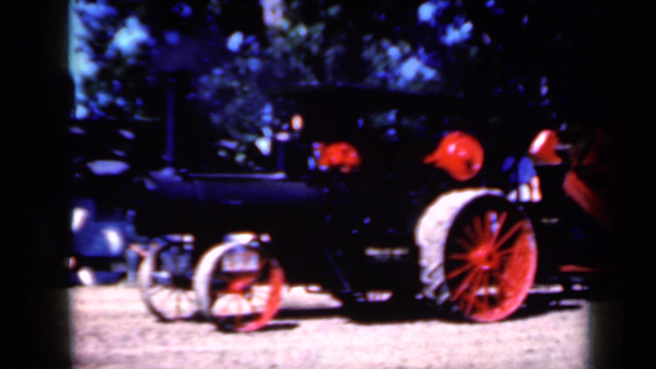Side view of the 1959 Iowa steam tractor footage, with red wheels, black boiler, and people visible near the operating area.