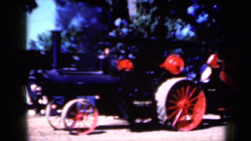 1959 Iowa home-movie frame of a steam tractor passing close by, with smoke above and people partially visible near the rear.