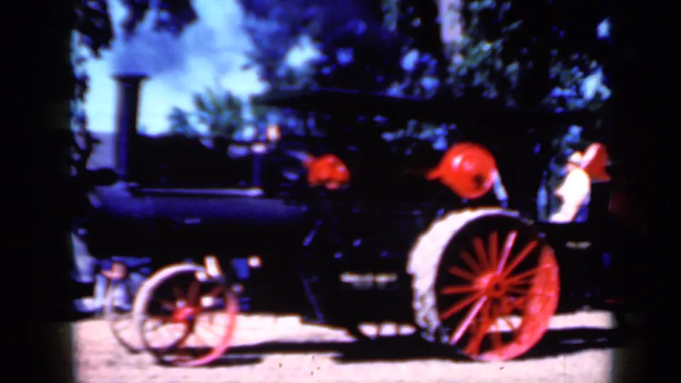Side-profile 8mm frame of the steam tractor in Iowa, with smoke rising and people visible near the right edge.