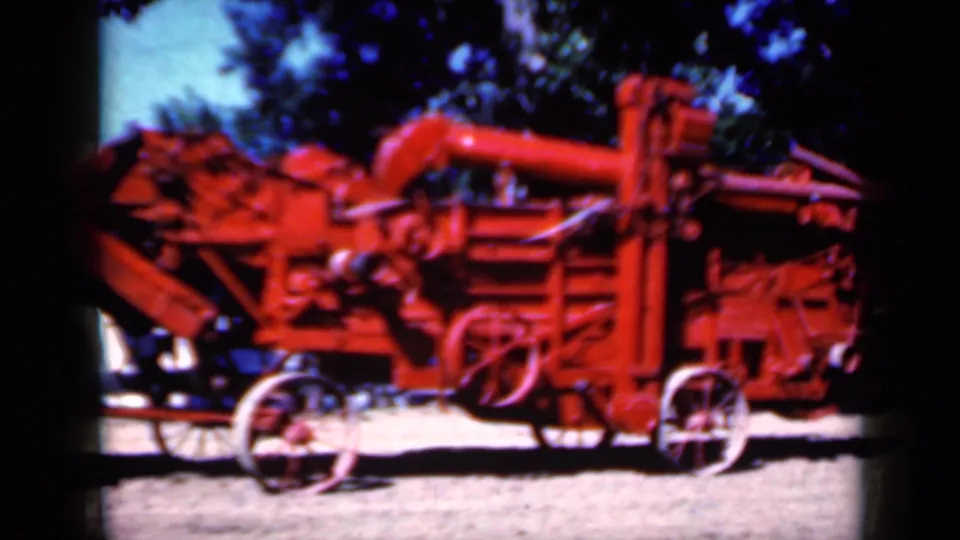 Final frame holds on the red agricultural machine outdoors in Iowa, with wheels, belt housings, trees, and bright ground visible.