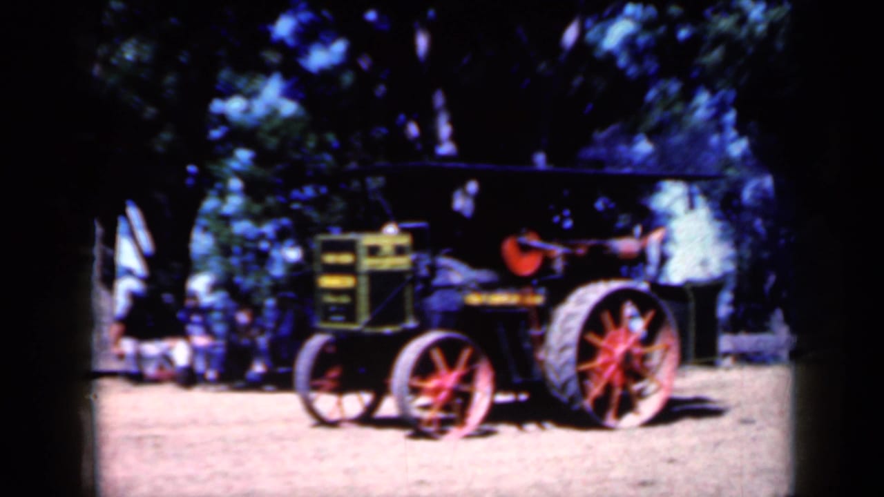 Vintage black and yellow tractor with red-spoked wheels parked on dirt under trees.
