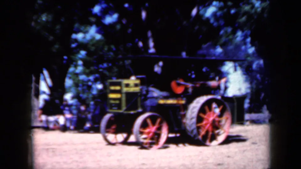 1959 Iowa 8mm frame showing a vintage tractor with red-spoked wheels parked in a shaded rural event area.