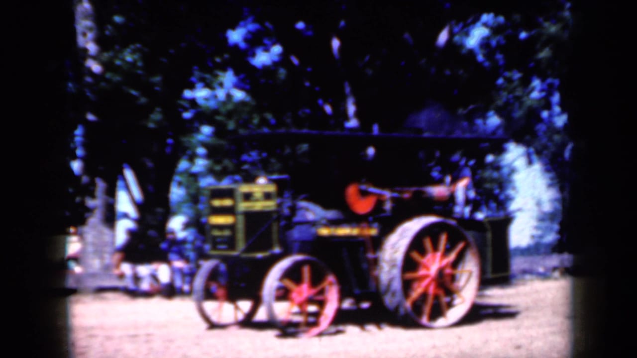 Side view of a vintage farm tractor at a 1959 Iowa rural gathering, with bright sun and deep tree shade.