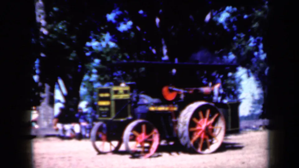 Side view of a vintage farm tractor at a 1959 Iowa rural gathering, with bright sun and deep tree shade.