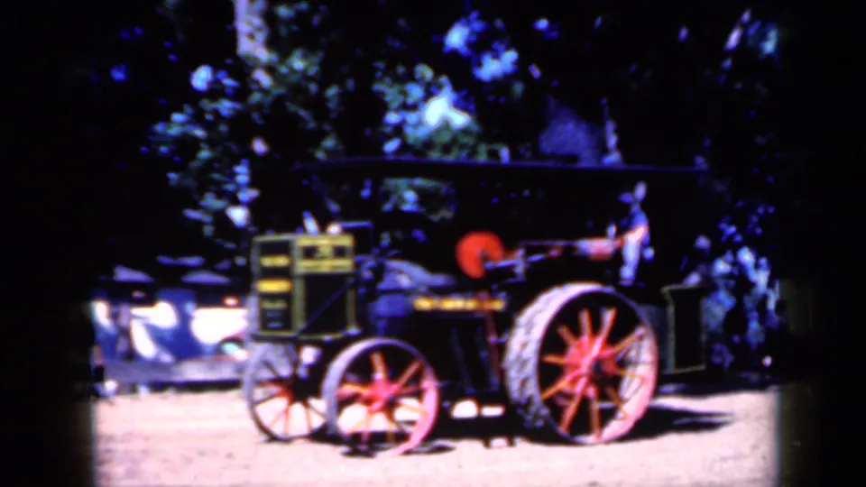 1959 Iowa home-movie frame of a vintage steam tractor under trees, with red wheels and high-contrast sunlight.