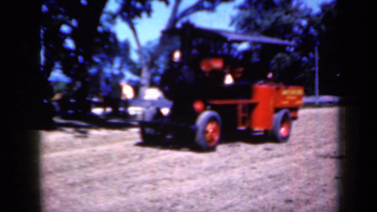 Steam engine seen from the side with a red wheel and yellow tank in a dirt clearing.