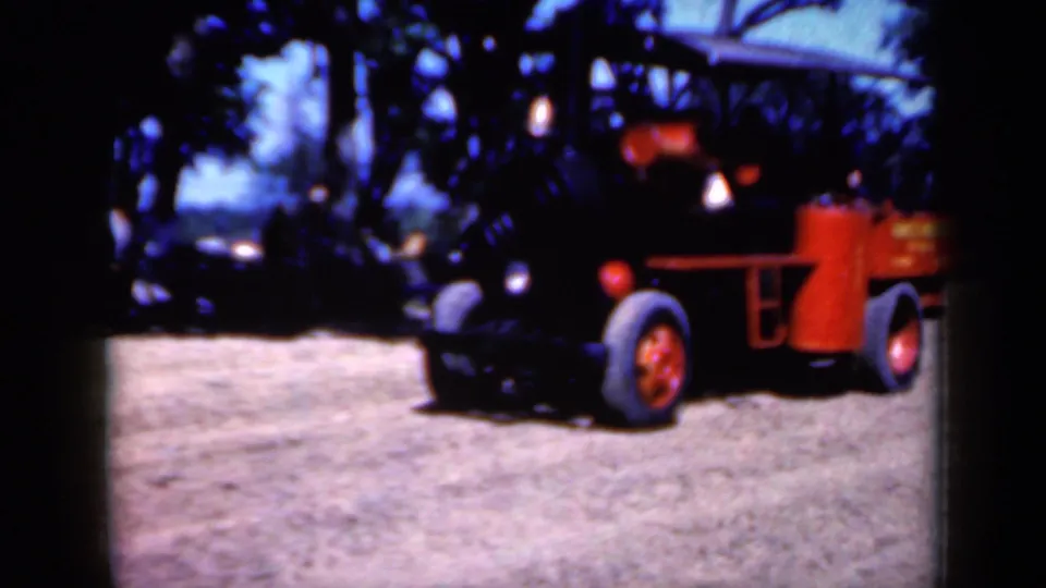Final 1959 Iowa frame shows the steam engine angled across the dirt field, with red wheels, yellow tank, trees, and parked cars visible.