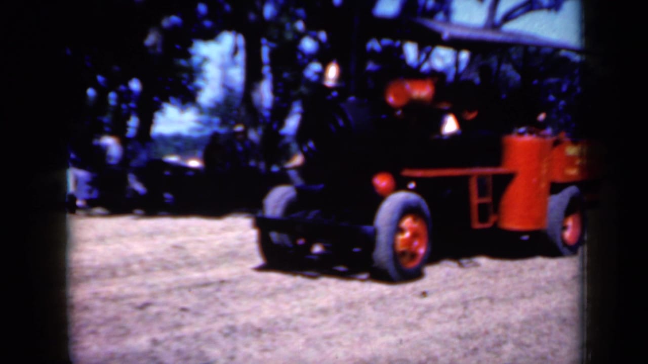 Red and black wheeled steam-style vehicle crossing a dirt area under trees.