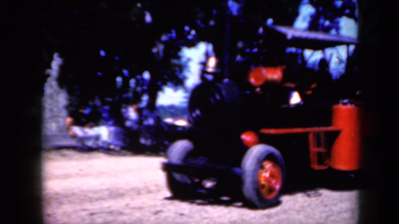 Small red and black train-like vehicle on tires near trees and dirt ground.
