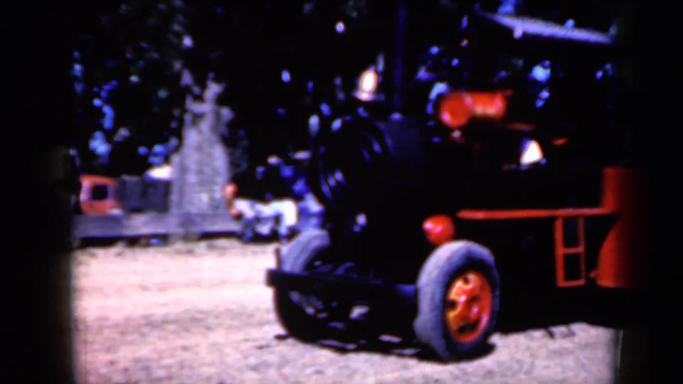 The home-movie frame shows a closer look at the red wheels, black engine body, and red fittings of the wheeled steam-style vehicle.