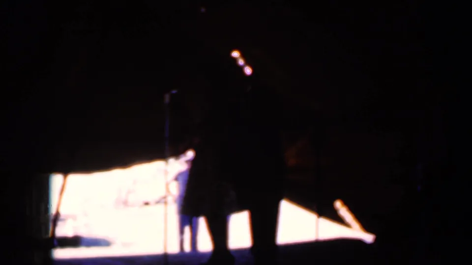 1959 Iowa home-movie frame showing shadowed visitors in a dark room, with a bright screen or opening illuminating their outlines.