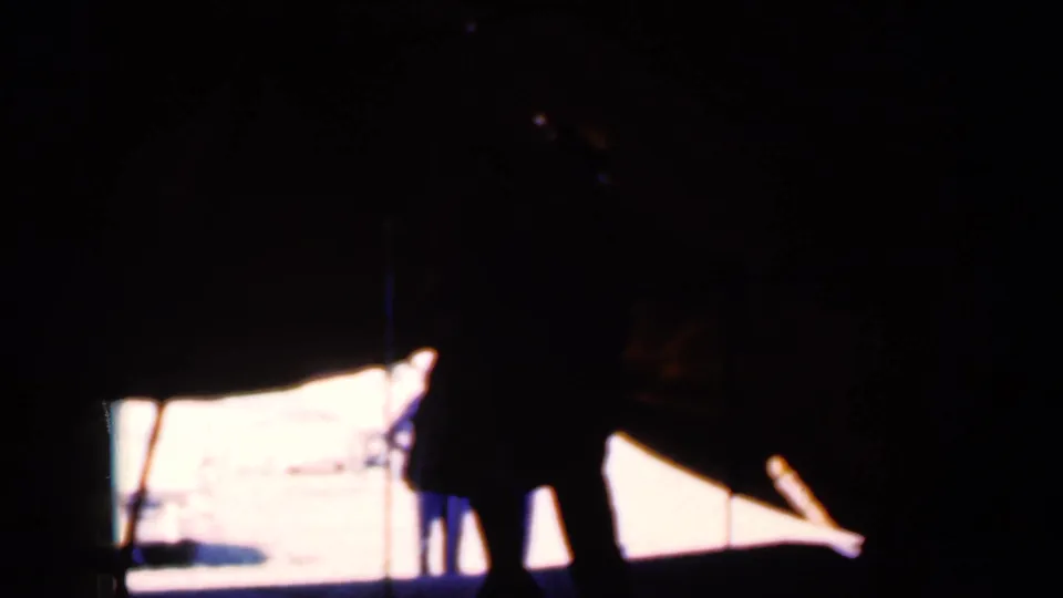 Dim 8mm frame from Iowa in 1959 with two silhouetted figures near a bright projected area, surrounded by heavy shadow.