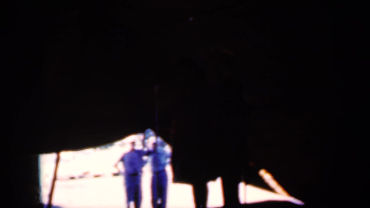 Two people stand near a brightly lit area beneath a dark tent or canopy.