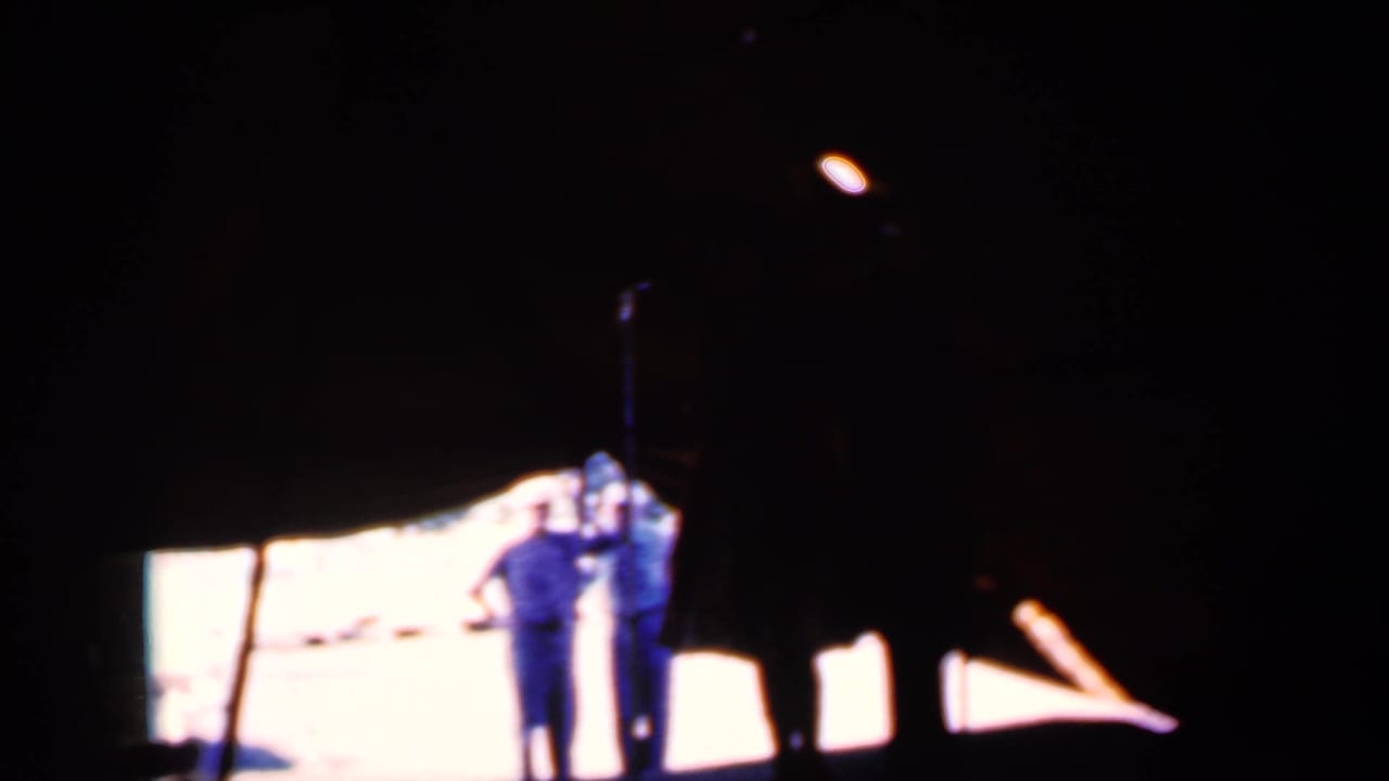 Two people remain near a bright opening with dark tent edges around them.