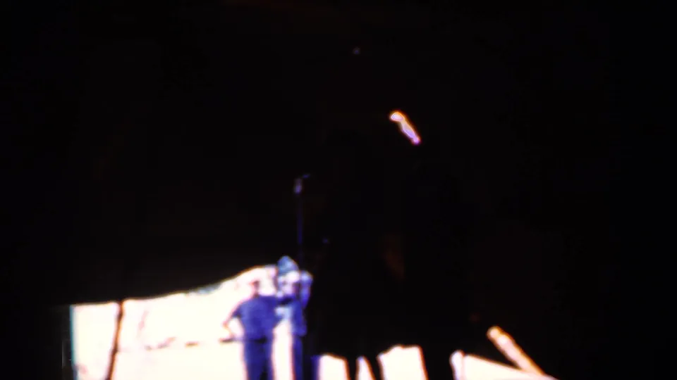 At the end of the 1959 Iowa clip, two adults stand at the edge of a bright area beneath a large dark tent or canopy shape.