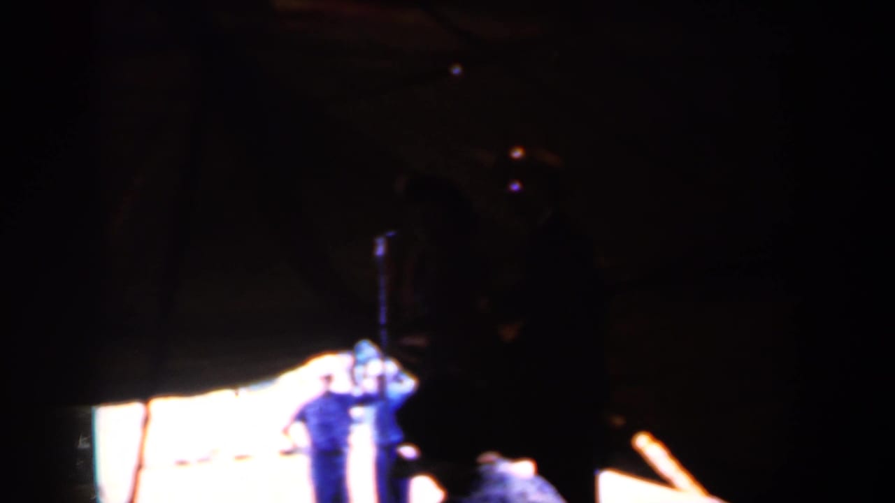 Silhouetted person at right with a lit stage area and microphone stand behind.