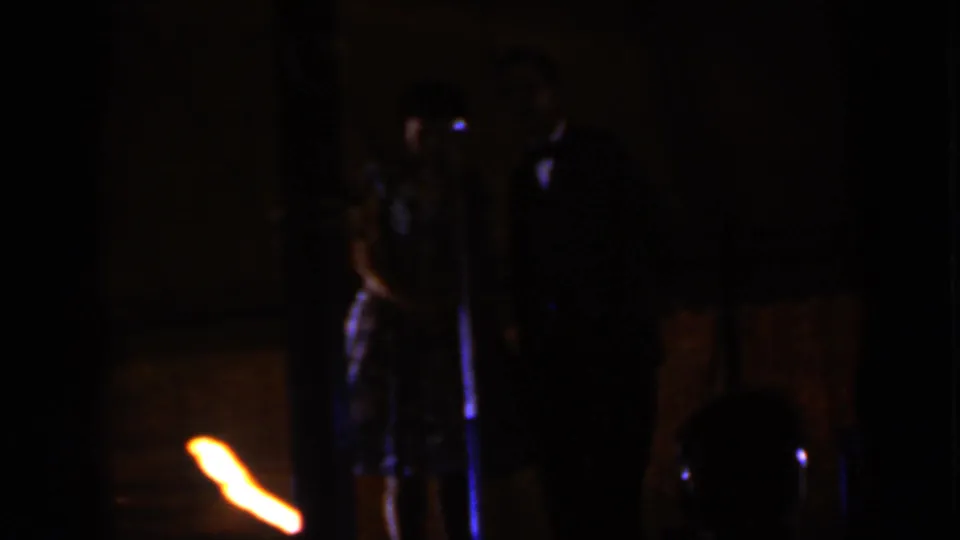 Low-light 8mm frame of a couple beside a microphone, seen from an audience position in Iowa, 1959.