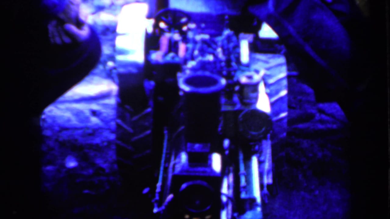 Blue-tinted close view of a small mechanical device with seated people partly visible around it.