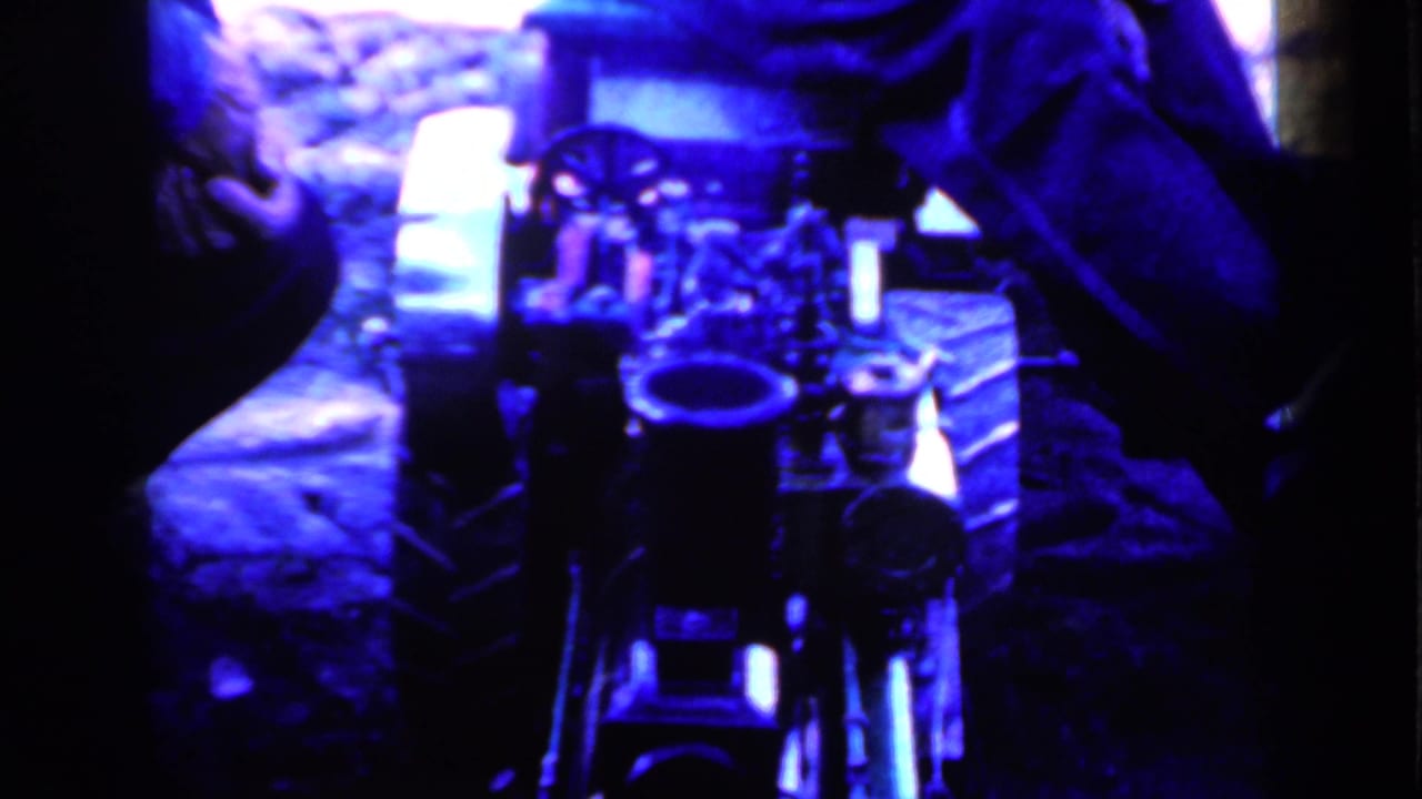 1959 Iowa home-movie frame with equipment centered low in the shot and seated adults partly visible around the edges.