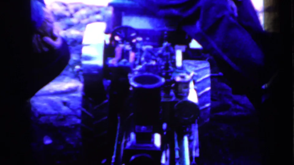 1959 Iowa home-movie frame with equipment centered low in the shot and seated adults partly visible around the edges.