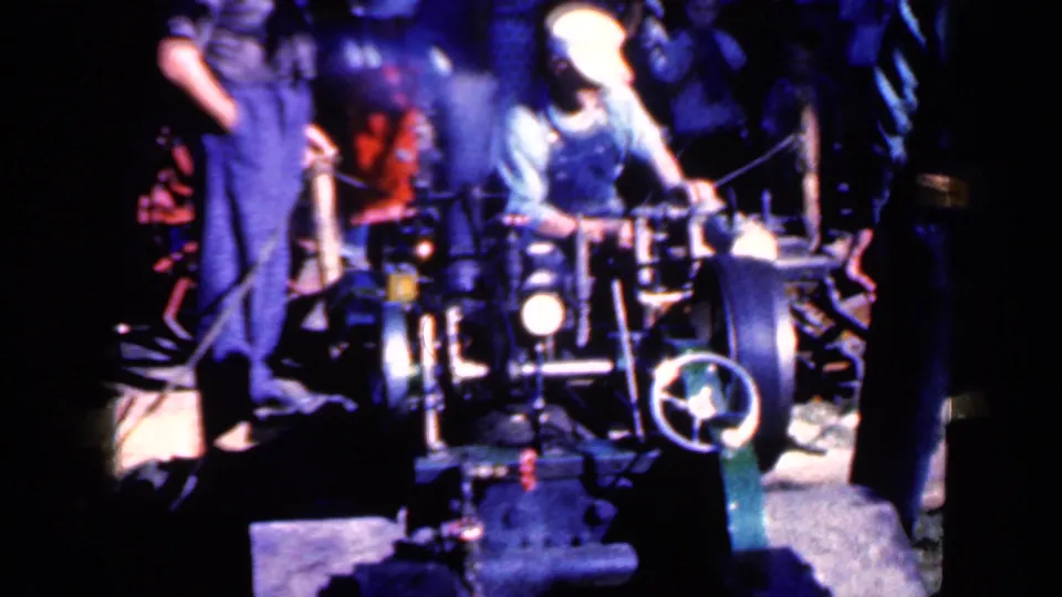 The 8mm frame shows an Iowa factory worker reaching across a machine, with another worker partly visible at the side.