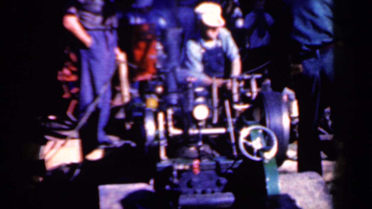The operator adjusts or guides the power-driven log trimmer while the assistant and spectators watch in the dim 1959 Iowa footage.
