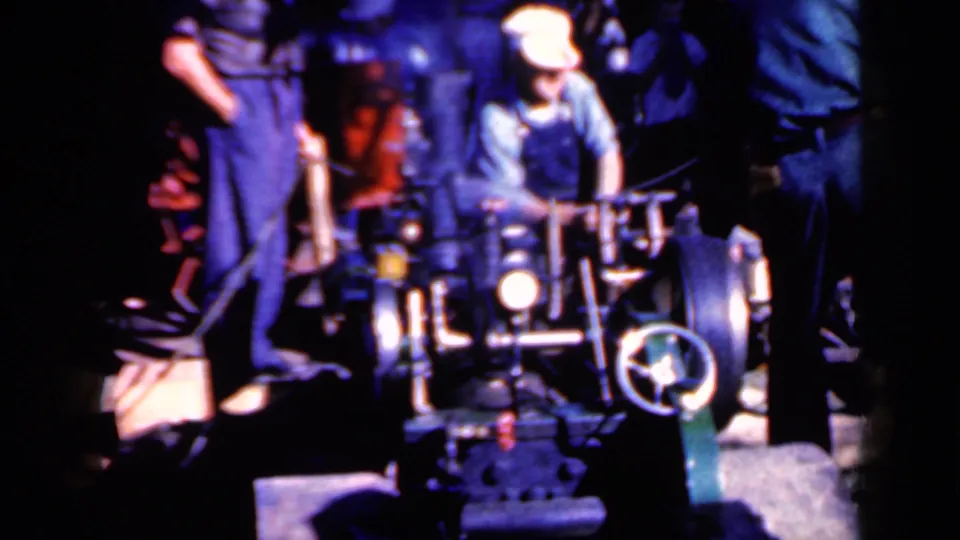 The operator adjusts or guides the power-driven log trimmer while the assistant and spectators watch in the dim 1959 Iowa footage.