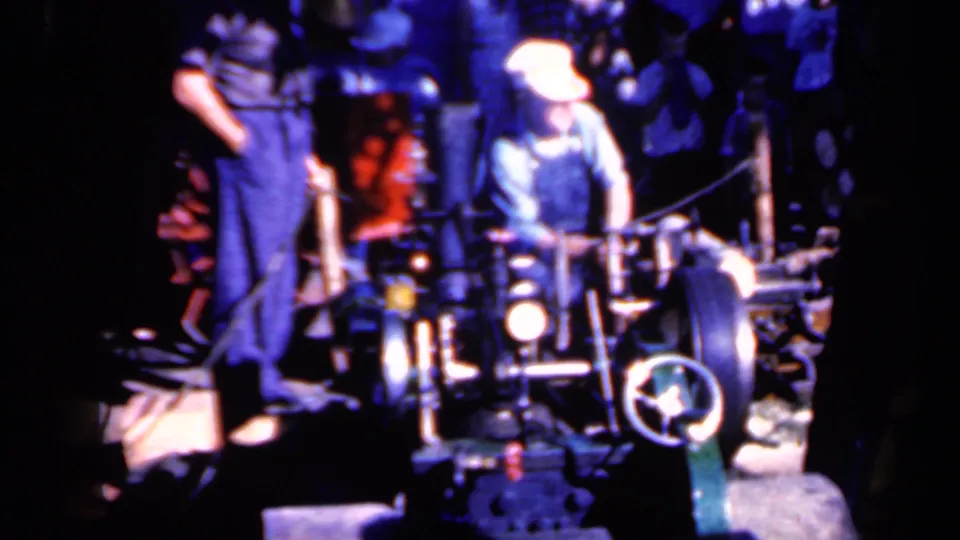 Capped operator and nearby assistant remain framed around the log-trimming machinery in saturated, grainy 8mm color.