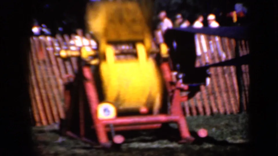 1959 Iowa home-movie frame with the yellow spinning apparatus blurred by motion, set in a red frame near a wooden fence and background visitors.