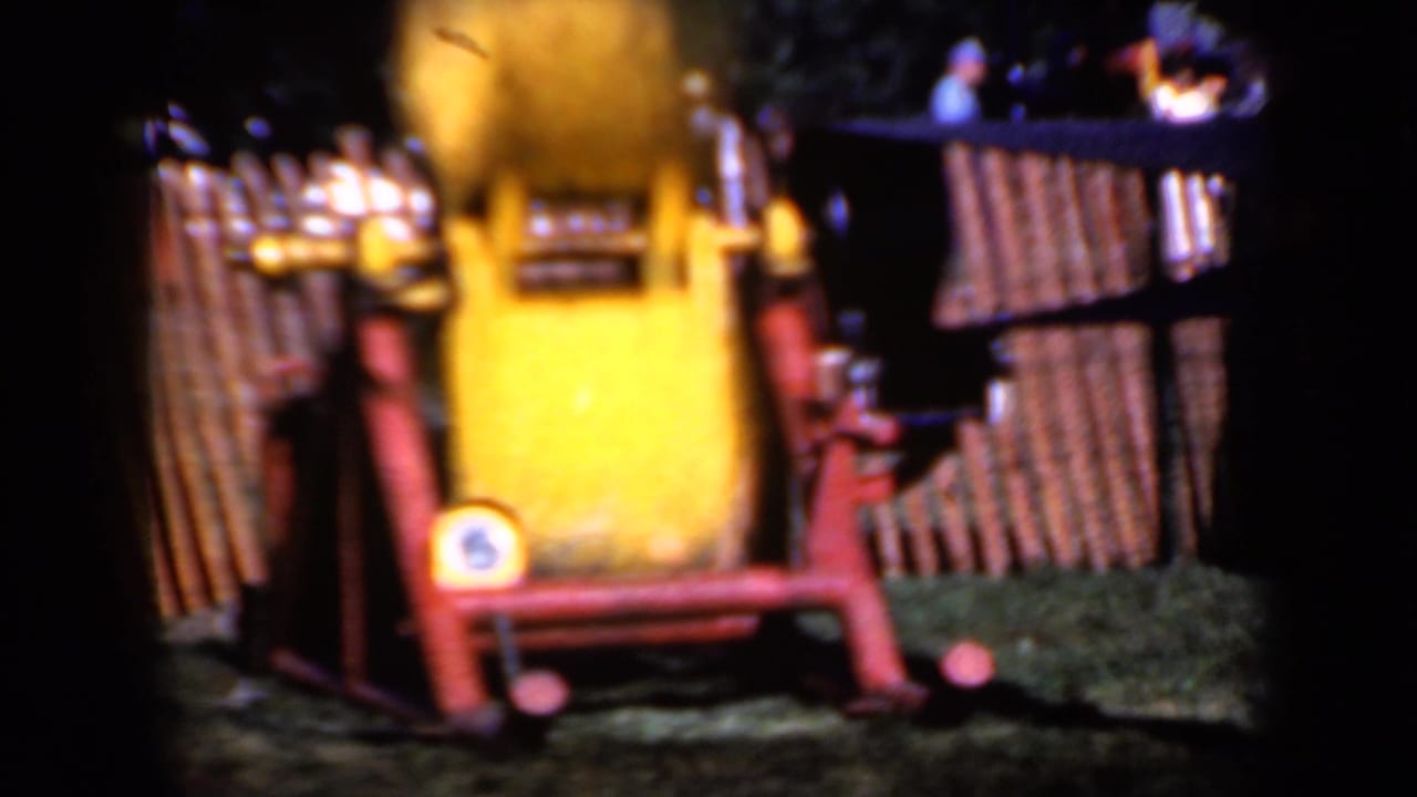 Yellow spinning machine on a red frame behind a wooden fence.