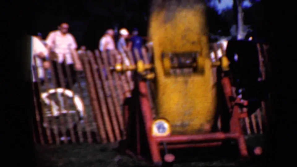 Spectators in light shirts and hats stand behind a wooden fence as the yellow machine operates at the Iowa event.