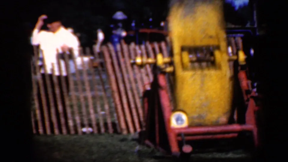 Home-movie frame from the Iowa train display showing spectators at a wooden fence and the yellow rail attraction close to the camera.