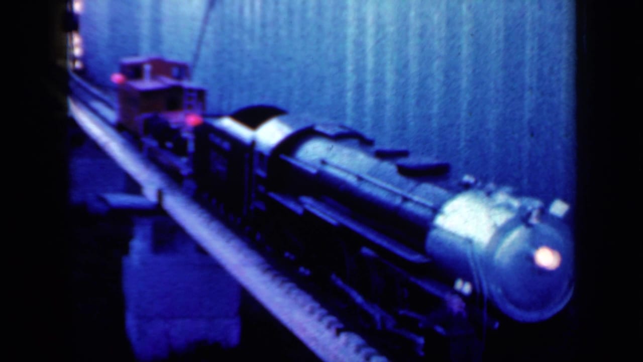 Toy steam locomotive and rail cars moving along a raised indoor track.