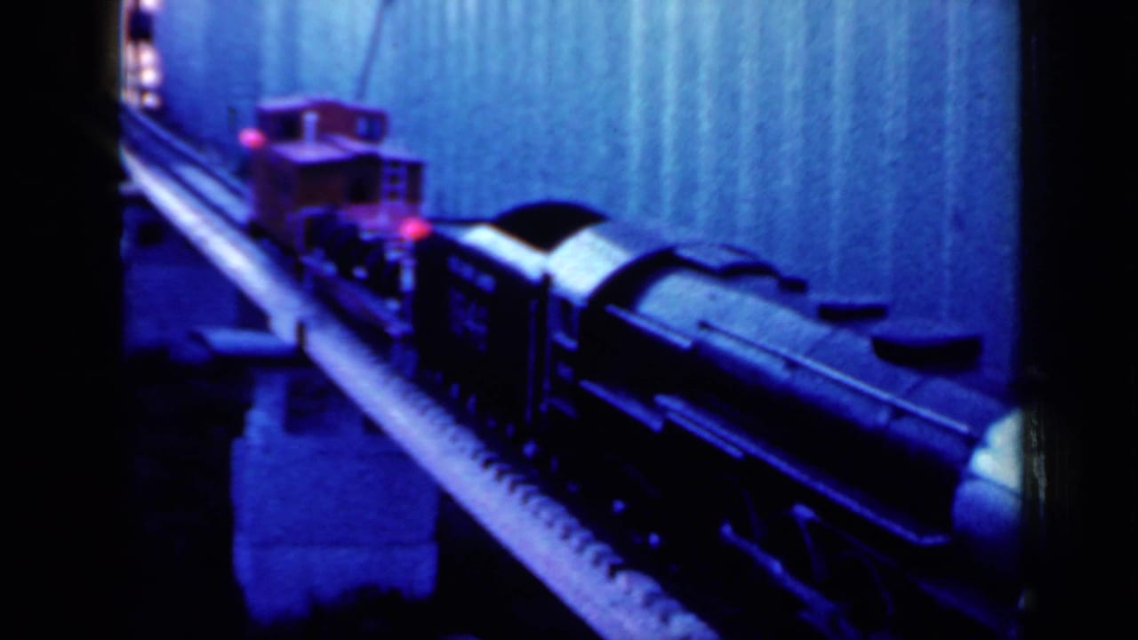 Model train cars pass close to the camera on an indoor track.