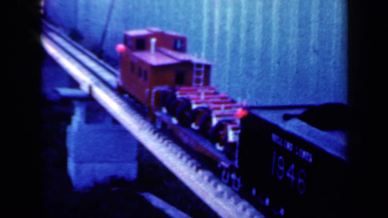 Red model caboose advances along the bridge beside a dark car marked 1946.