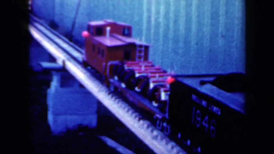 The miniature train continues across the bridge, with the red caboose and a dark car marked 1946 visible in the frame.