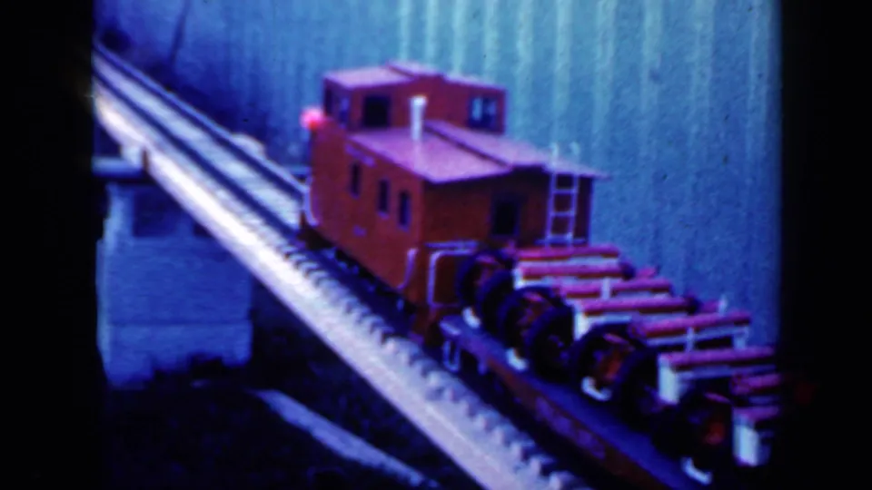 Near the end of the clip, the red caboose dominates the 1959 Iowa home-movie frame as it crosses the narrow bridge.