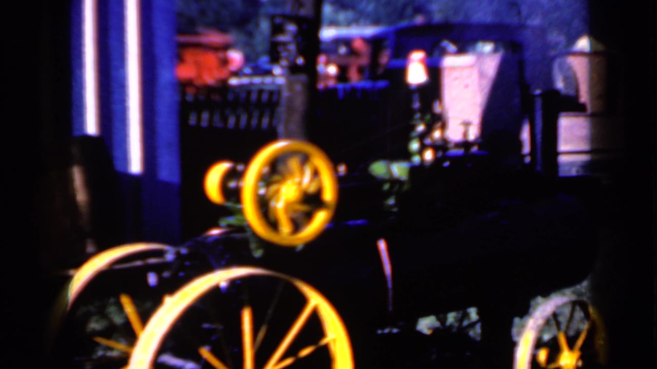 Dark, soft-focused view of a wheeled vehicle or machine with yellow wheels near a building or trailer area.