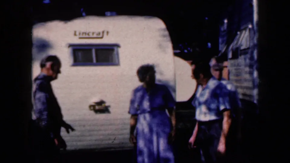 Three adults remain near the white Lincraft trailer in the 1959 Iowa home movie, with strong contrast and shadow shaping the frame.