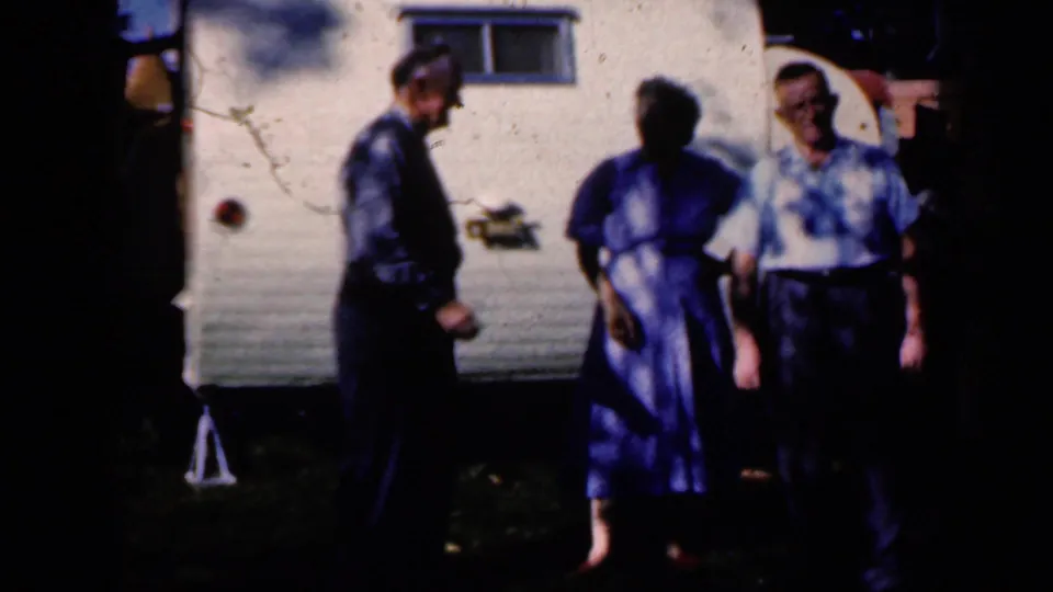 Three adults stand before the white Lincraft trailer, with strong tree shadows and soft 8mm color typical of the 1959 home-movie clip.